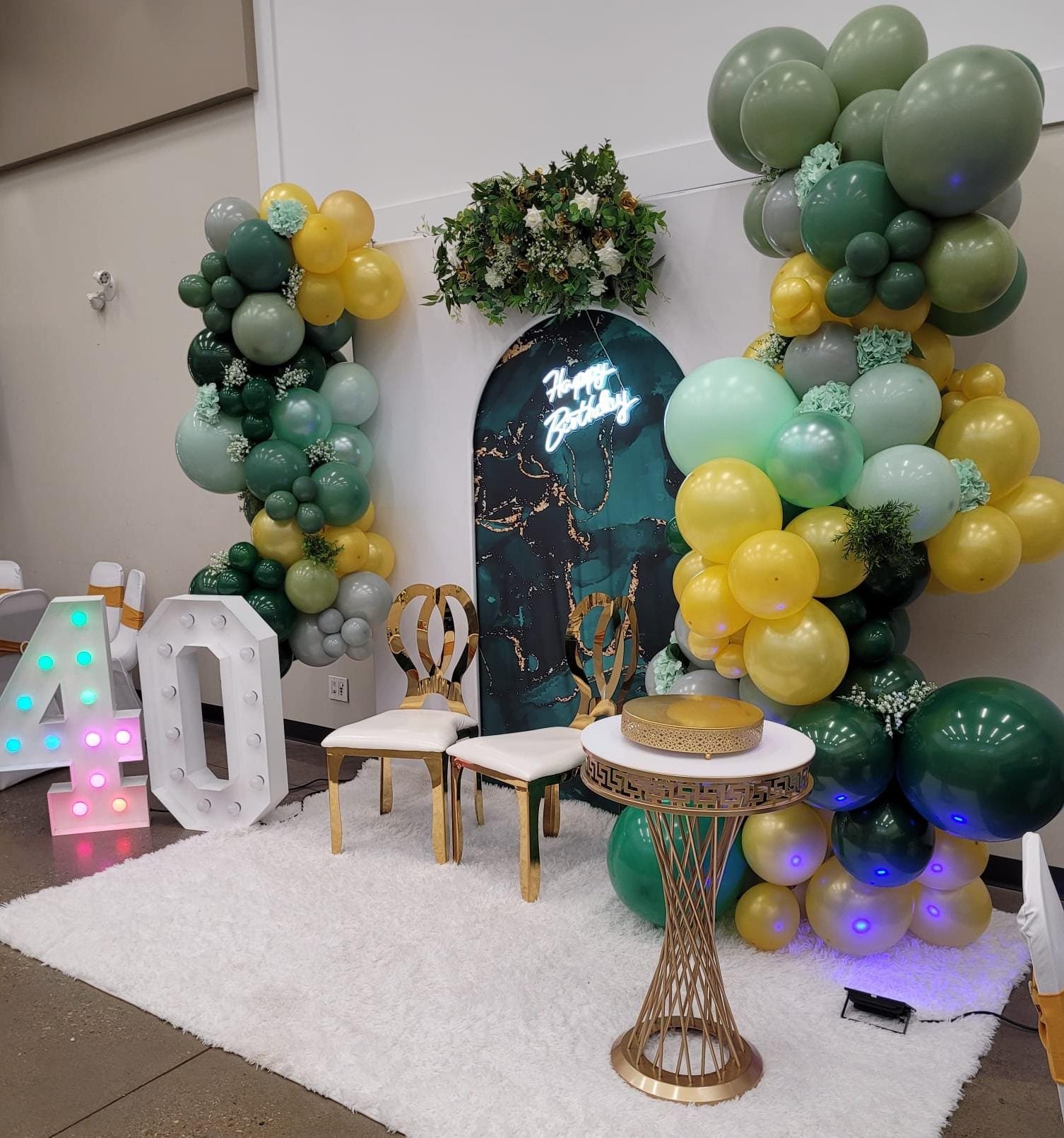 Arched stage backdrop with green and gold balloon garland and gold chairs