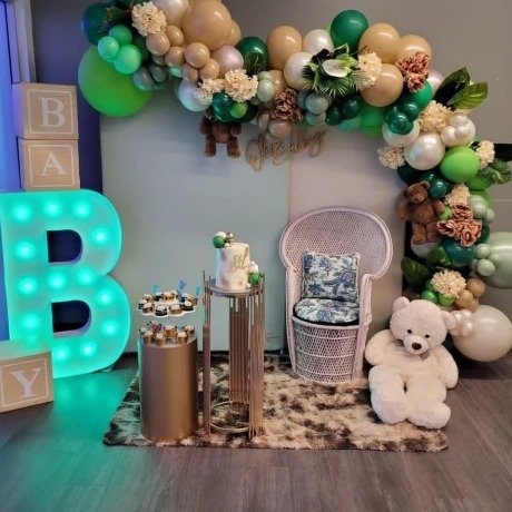 Baby shower backdrop with green and neutral balloon arch, marquee letter and teddy bears
