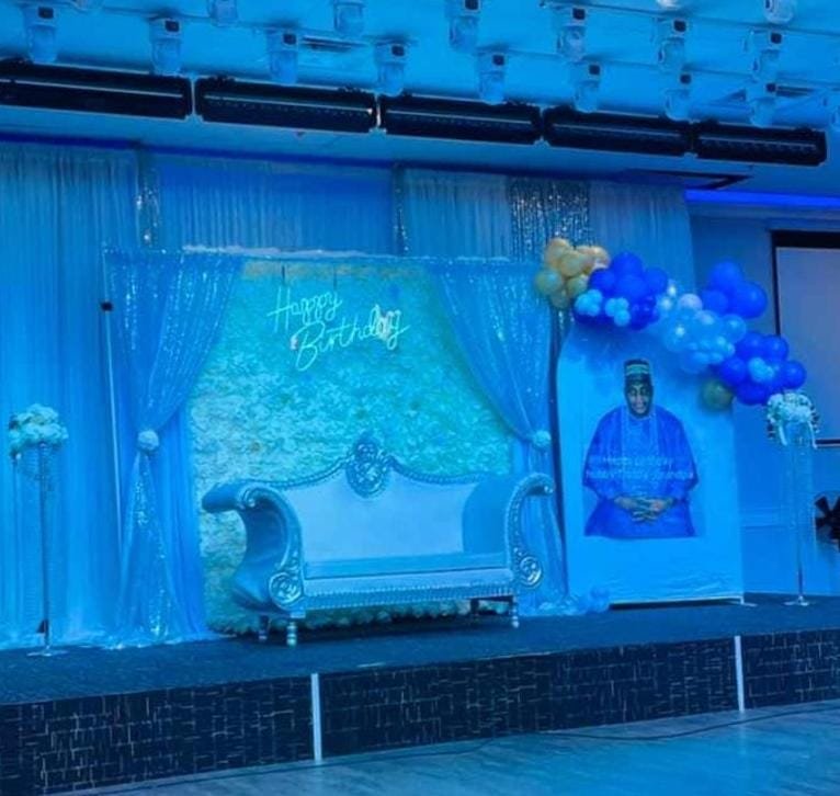 Blue-lit birthday stage with flower wall, silver sofa and balloon garland