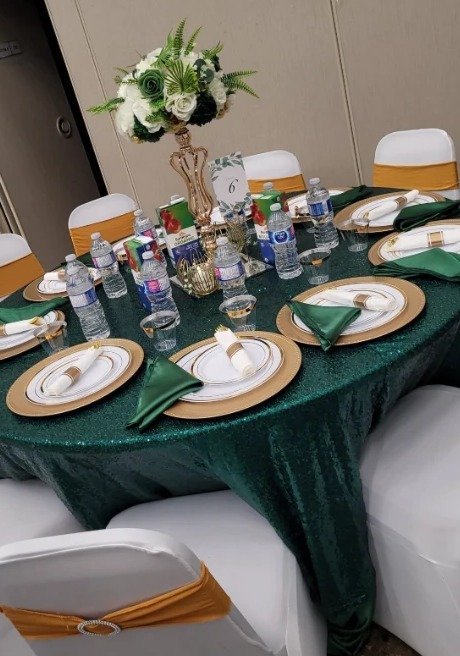 Round table set with emerald sequin linen, gold chargers and floral centrepiece