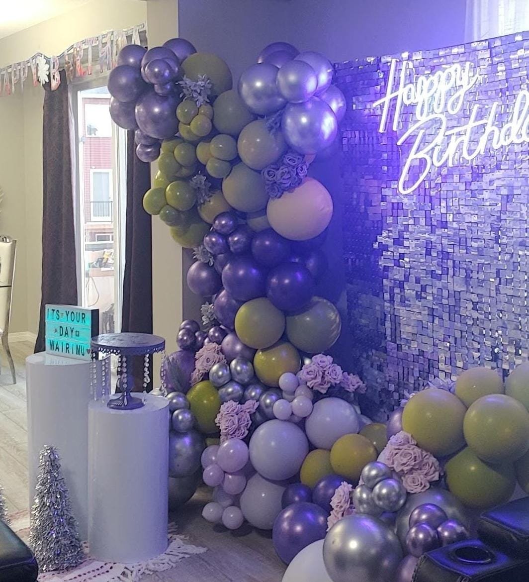 Purple, olive and silver balloon garland beside a shimmer wall with neon sign